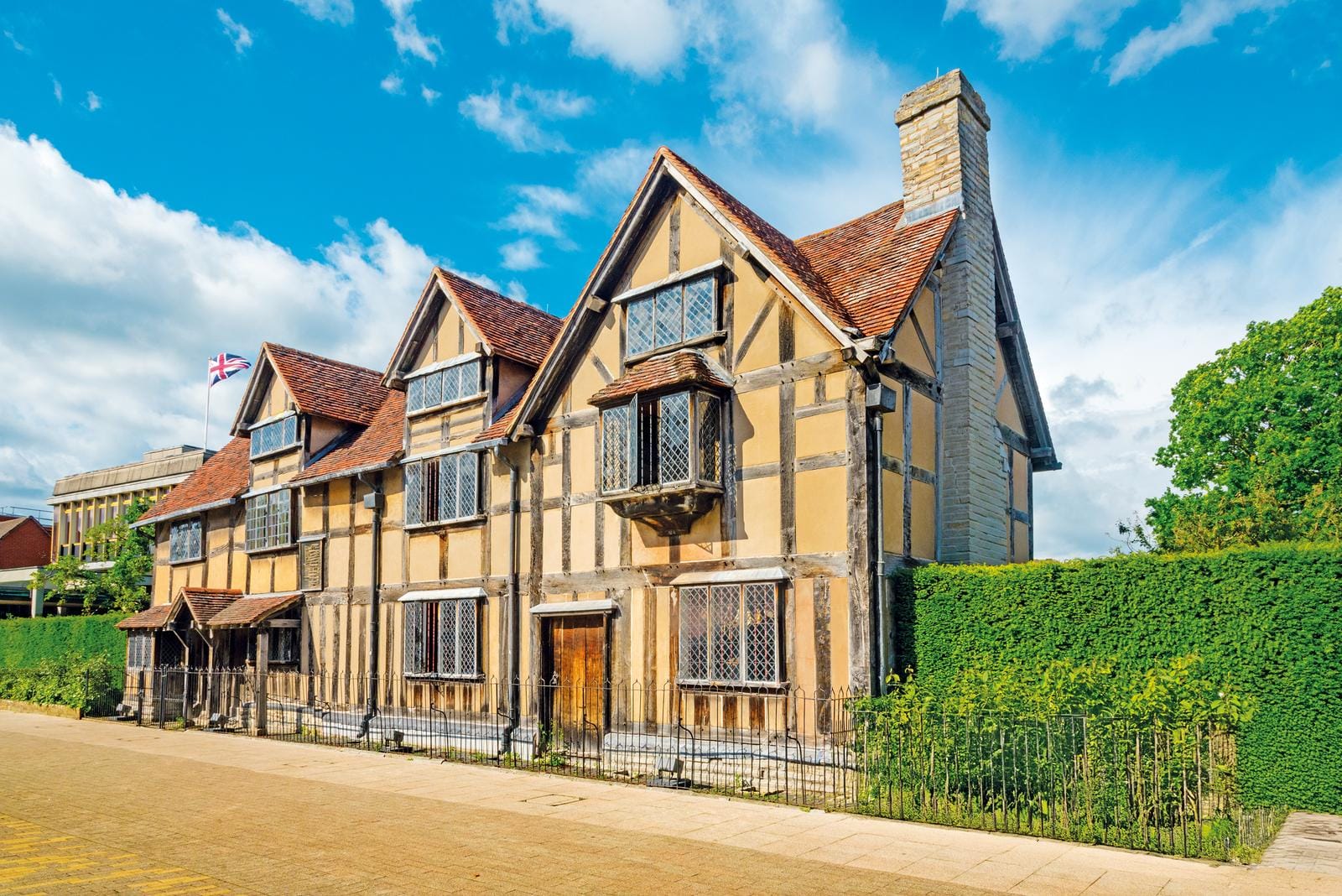Fachwerkhaus mit Holzbalken, Ziegeldach, England-Flagge, blauer Himmel, grüne Hecke.