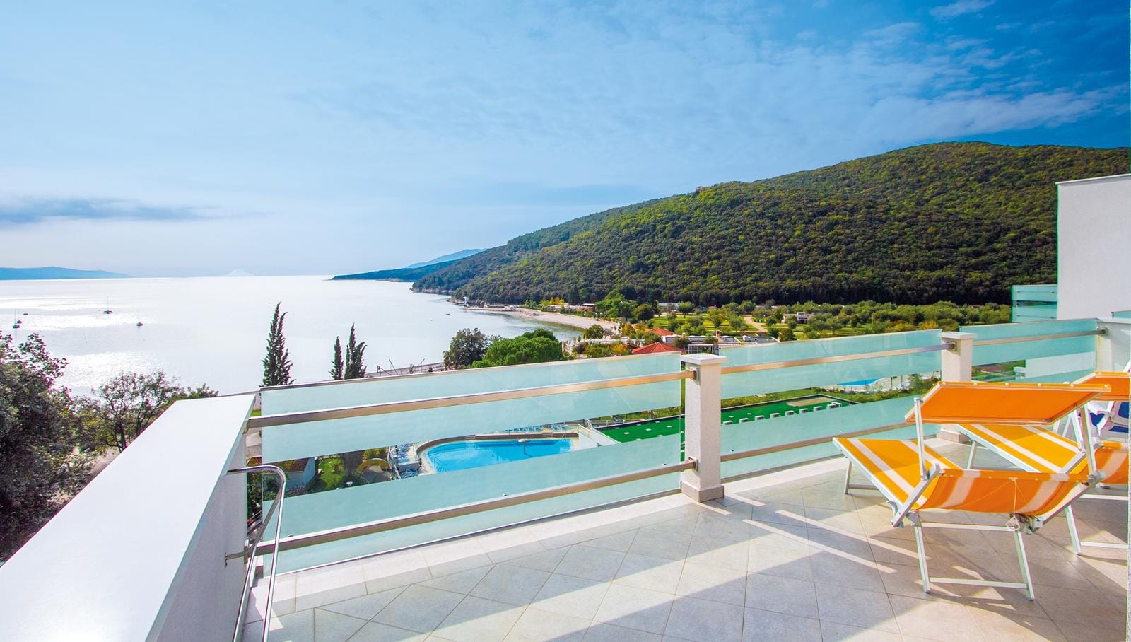 Balkon mit Meerblick, orange Liegestühle, üppige Hügel im Hintergrund.
