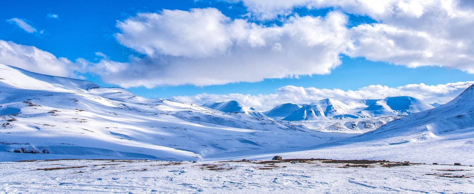 Verschneite Berge unter blauem Himmel mit weißen Wolken, ruhige Winterlandschaft.