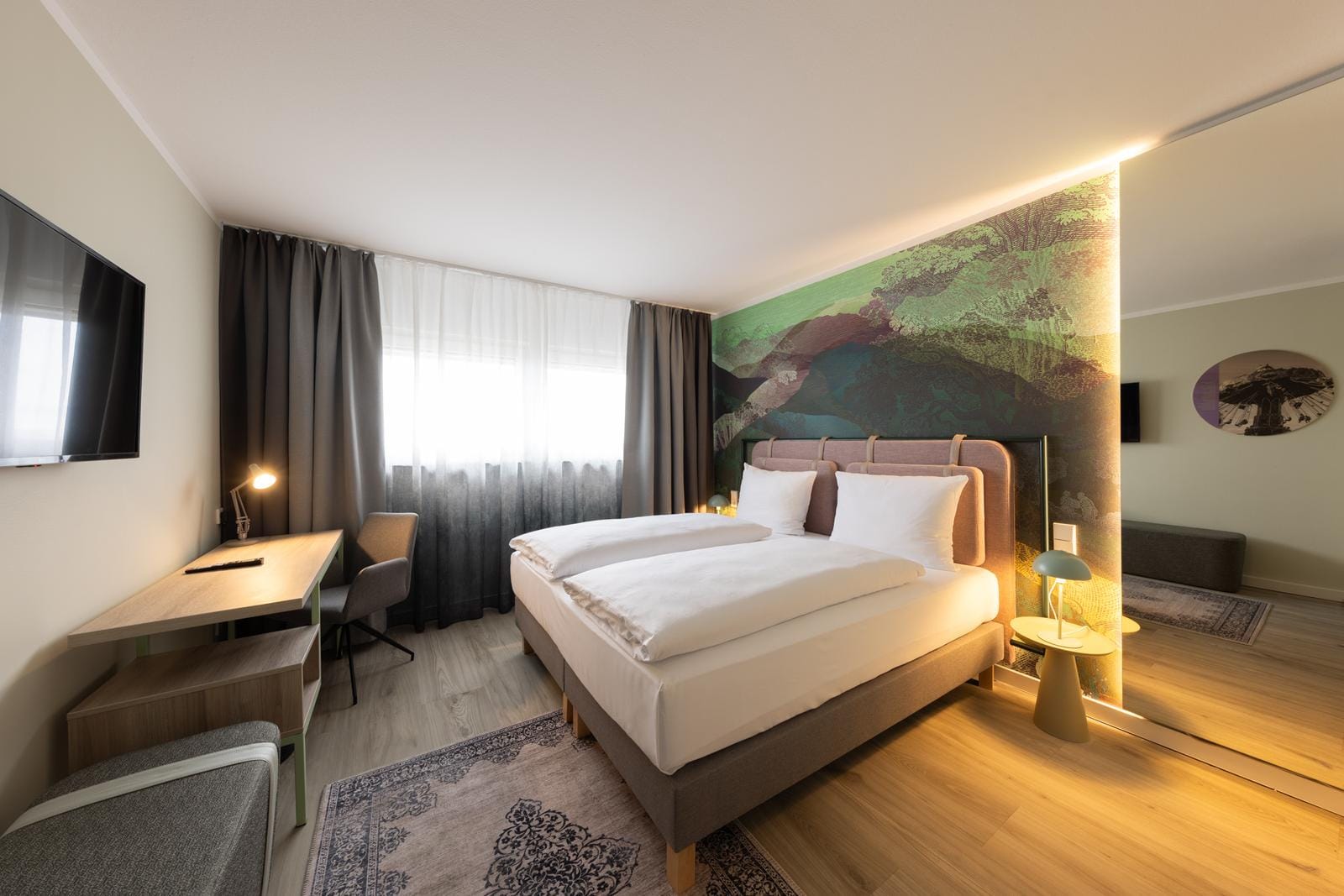 Modernes Hotelzimmer mit Doppelbett, Schreibtisch, Wandkunst und warmem Licht.