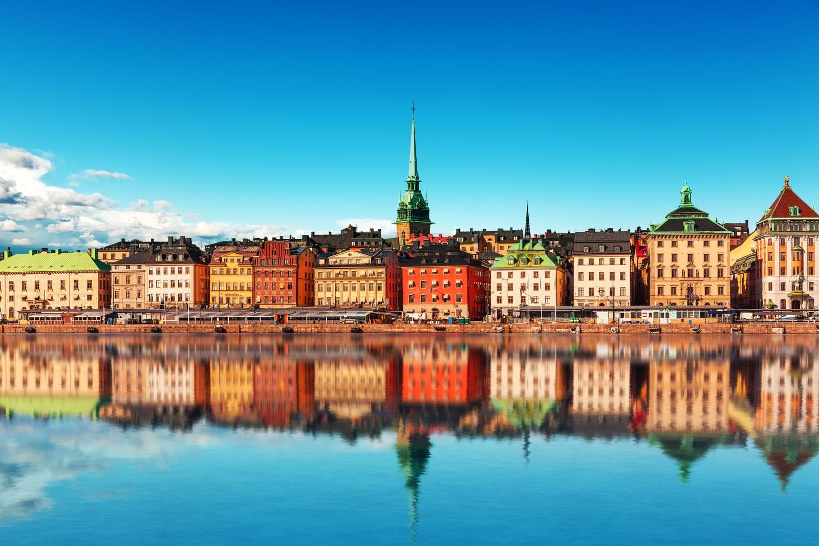Bunte Altstadtfassaden und Kirchen in Stockholm, Schweden spiegeln sich im Wasser.