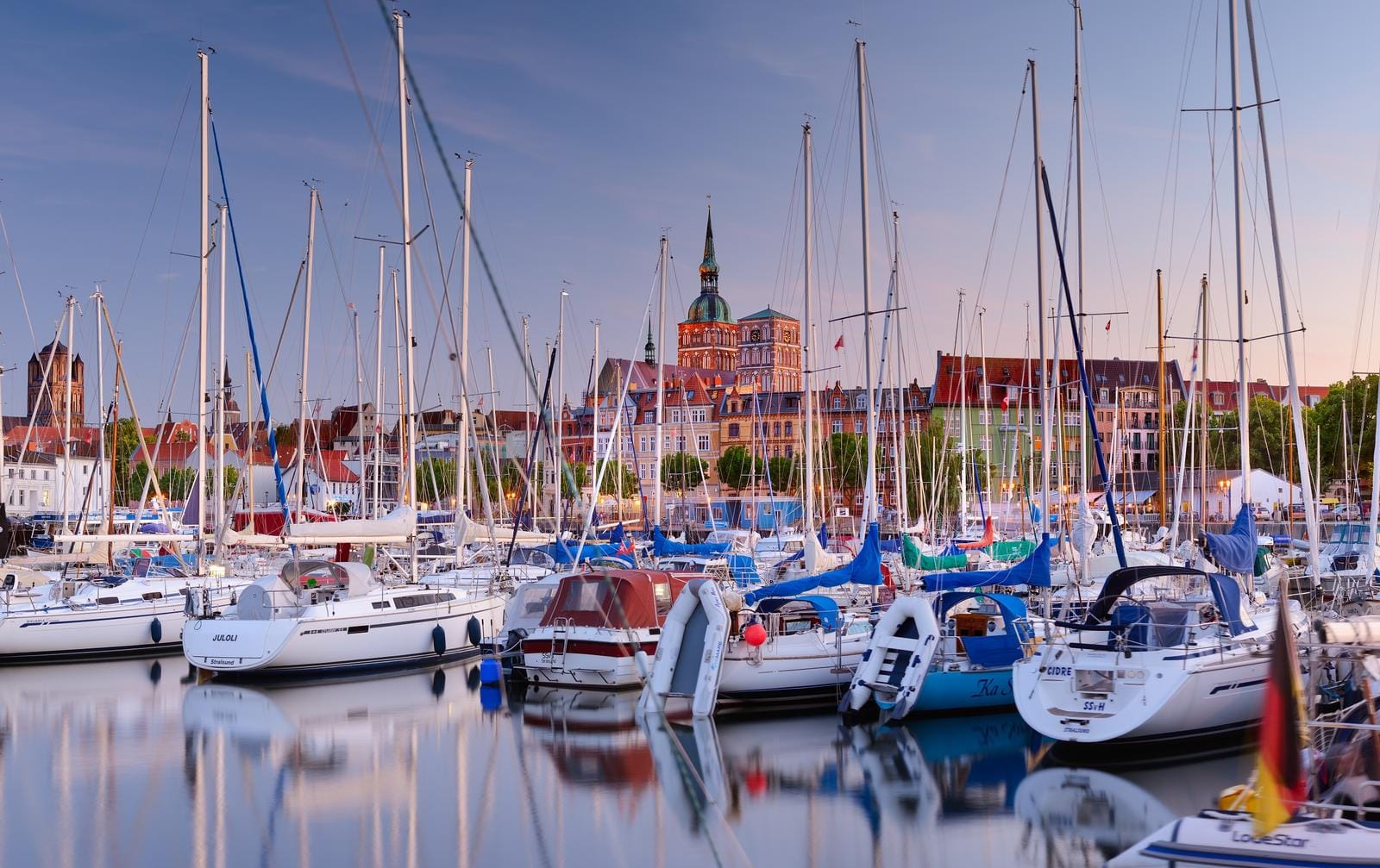 Yachthafen bei Sonnenuntergang in Stralsund, Deutschland, mit historischen Gebäuden.