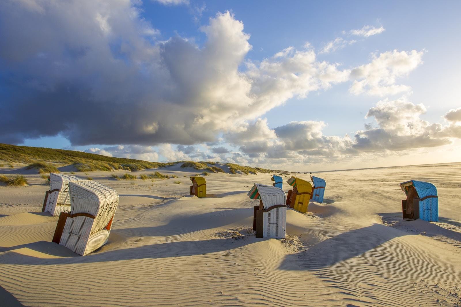 Sanddünen mit bunten Strandkörben unter bewölktem Himmel auf einer Nordseeinsel.