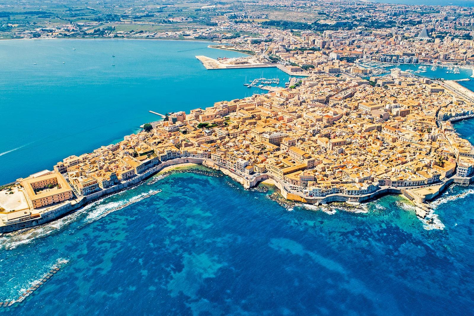Luftaufnahme von Ortigia, Syrakus, Italien, mit blauem Meer und historischen Gebäuden.