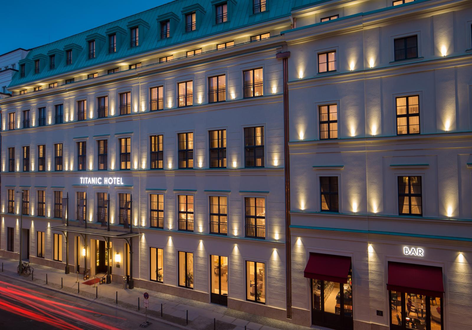 Elegantes Hotelgebäude bei Nacht, beleuchtet, klassischer Stil, großflächige Fenster.