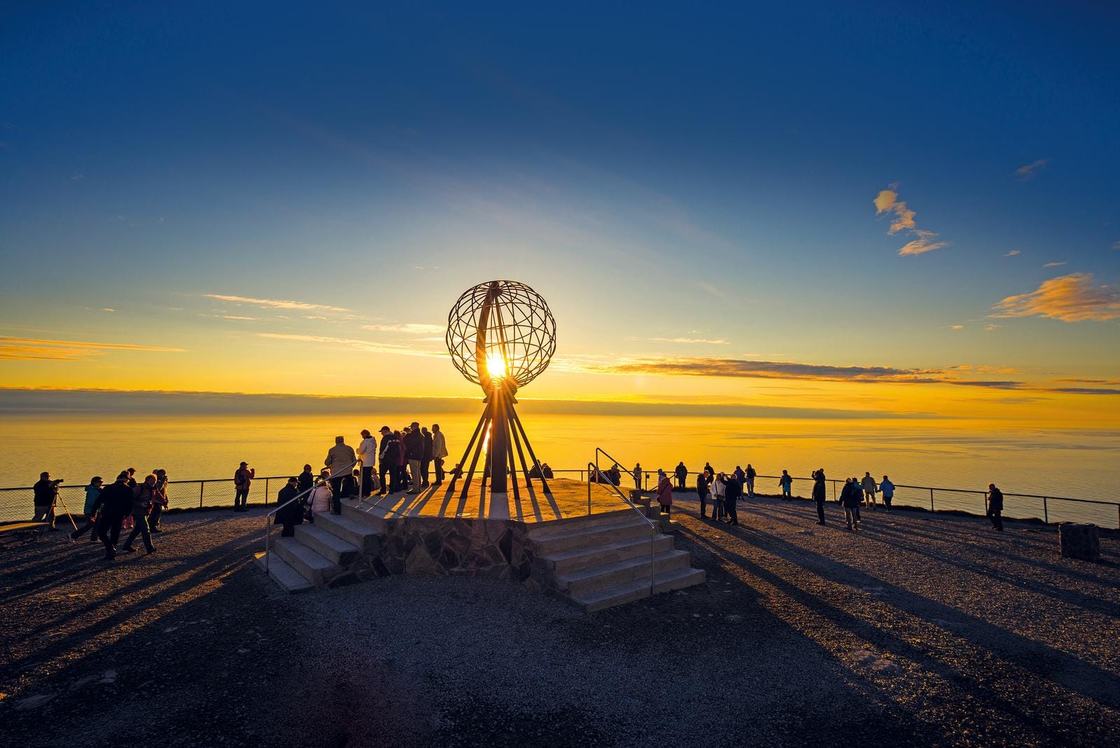 Besucher am Nordkap, Norwegen, vor Sonnenuntergang, mit Globusskulptur im Vordergrund.