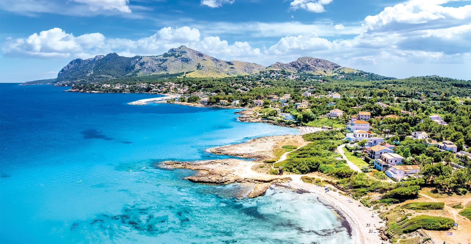 Küstenstadt auf Mallorca mit klarem, blauem Wasser und grünen Hügeln im Hintergrund.