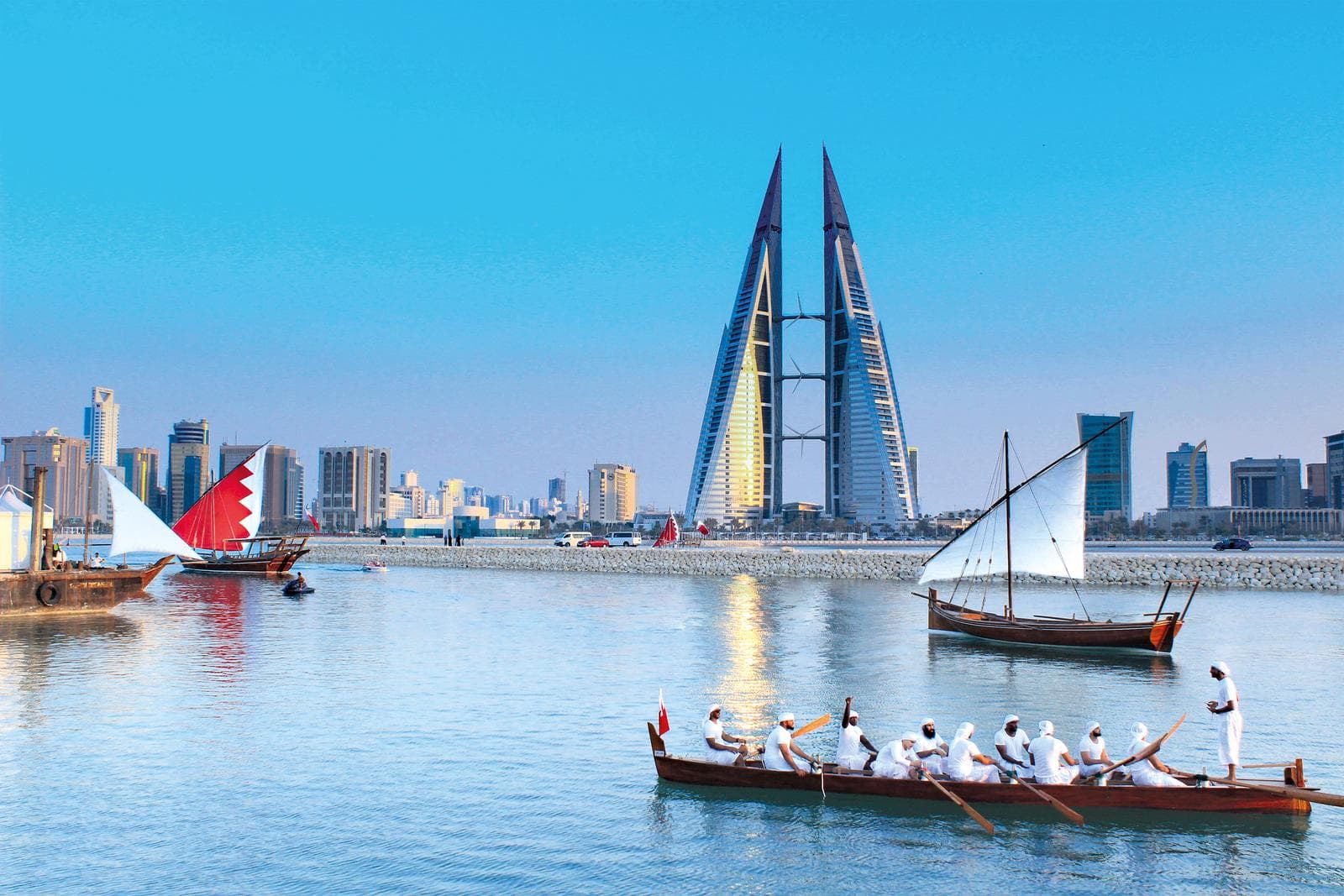 Traditionelle Boote vor der modernen Skyline von Manama, Bahrain, bei klarem Himmel.