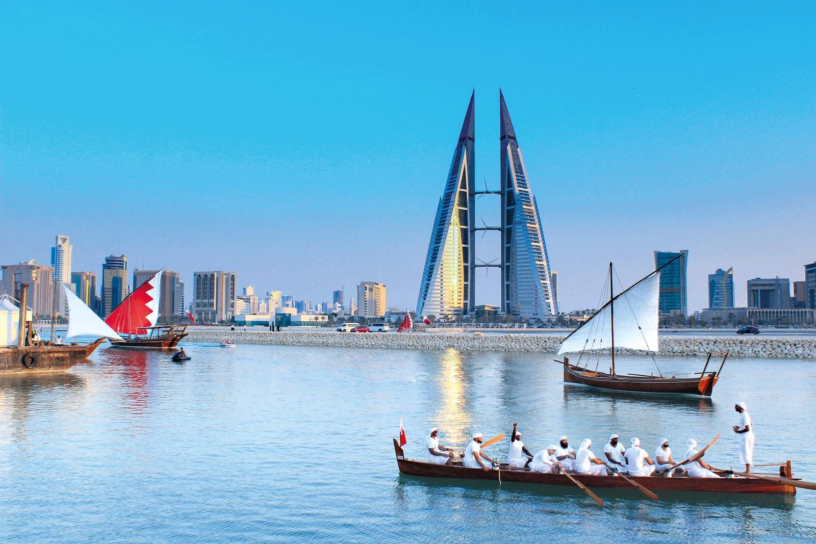 Traditionelle Boote vor der modernen Skyline von Manama, Bahrain, bei klarem Himmel.