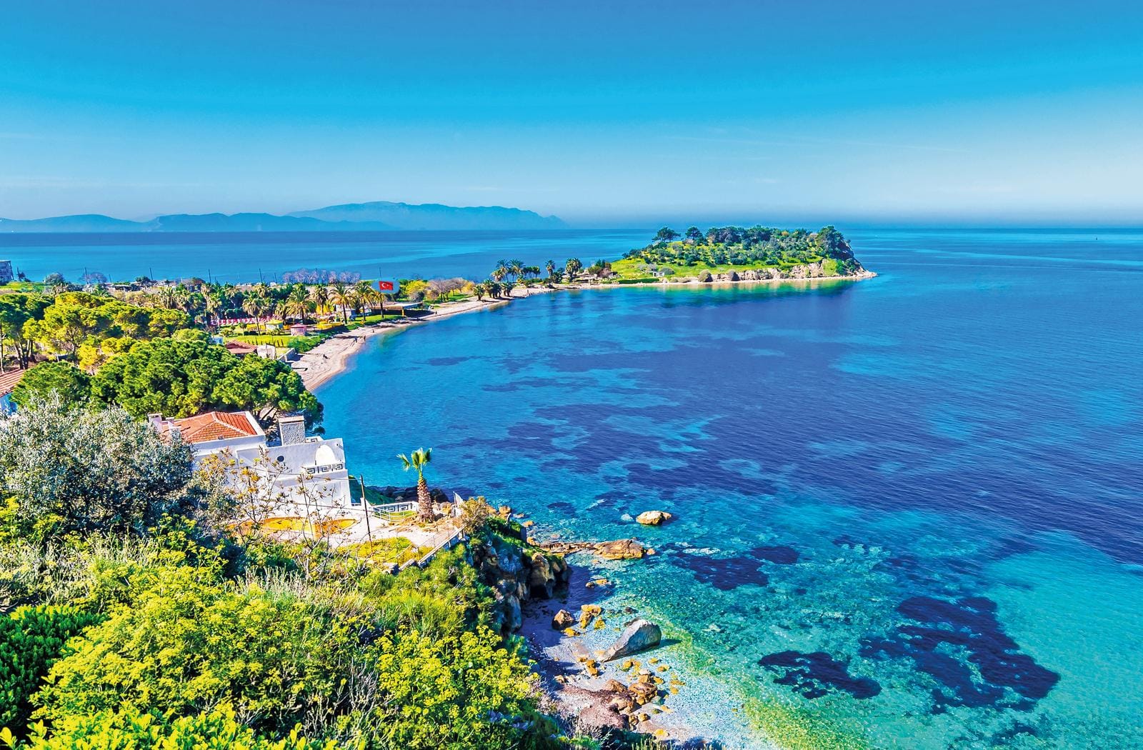 Türkische Küste mit blauem Meer und grüner Halbinsel, klares Wasser, sonniger Himmel.