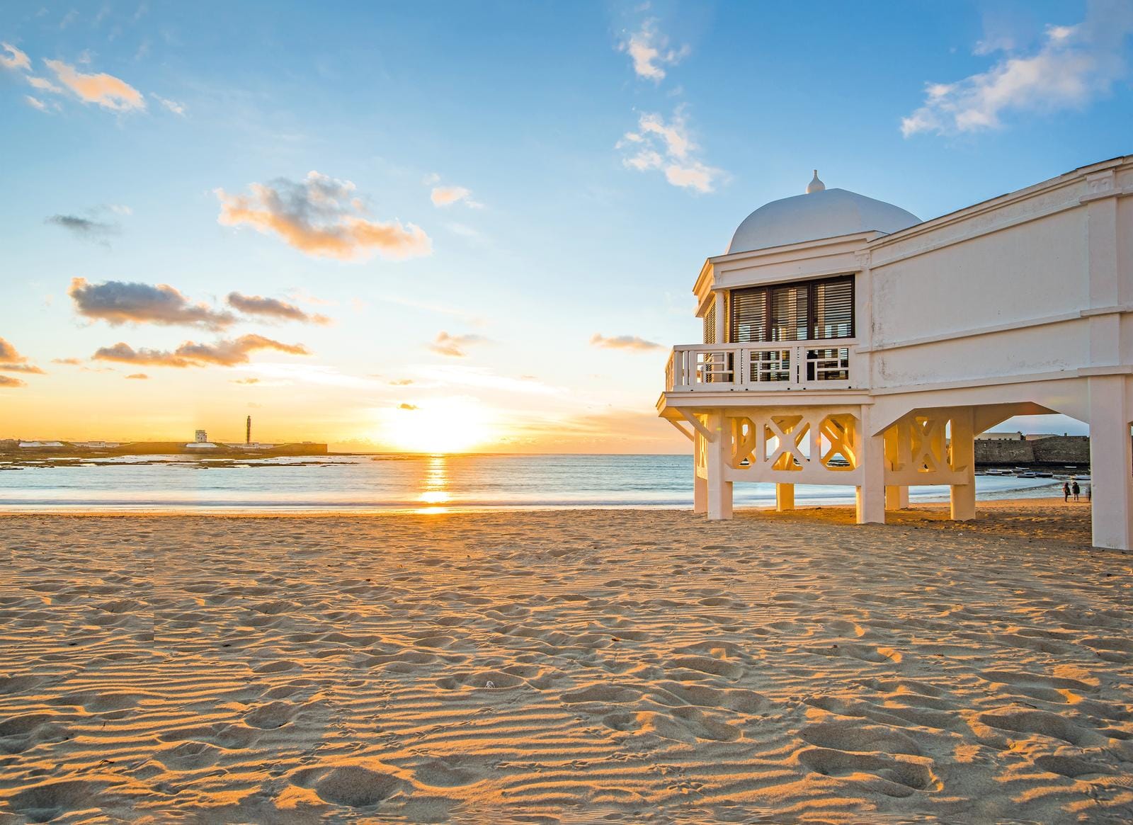 Sonnenuntergang am Strand von Cádiz, Spanien, mit weißem Pavillon und warmem goldenen Licht.