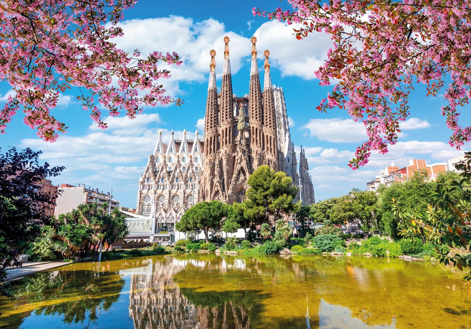 Beeindruckende Sagrada Familia in Barcelona mit blühenden Bäumen und klarem Himmel.