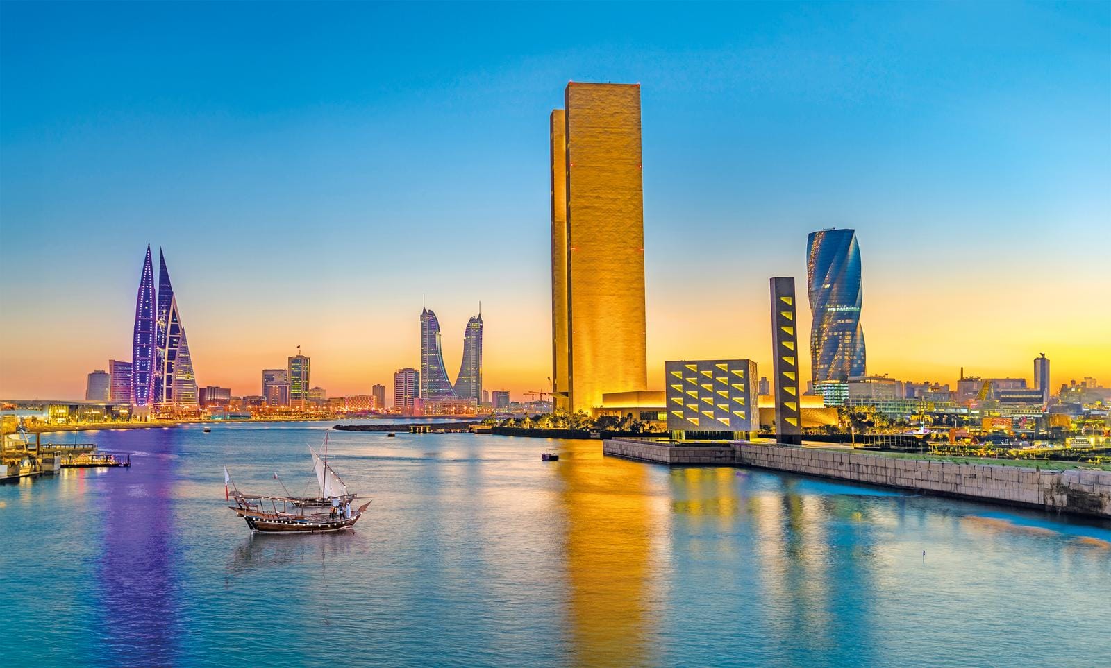 Moderne Skyline von Manama, Bahrain, bei Sonnenuntergang mit traditionellen Dhau-Booten im Wasser.