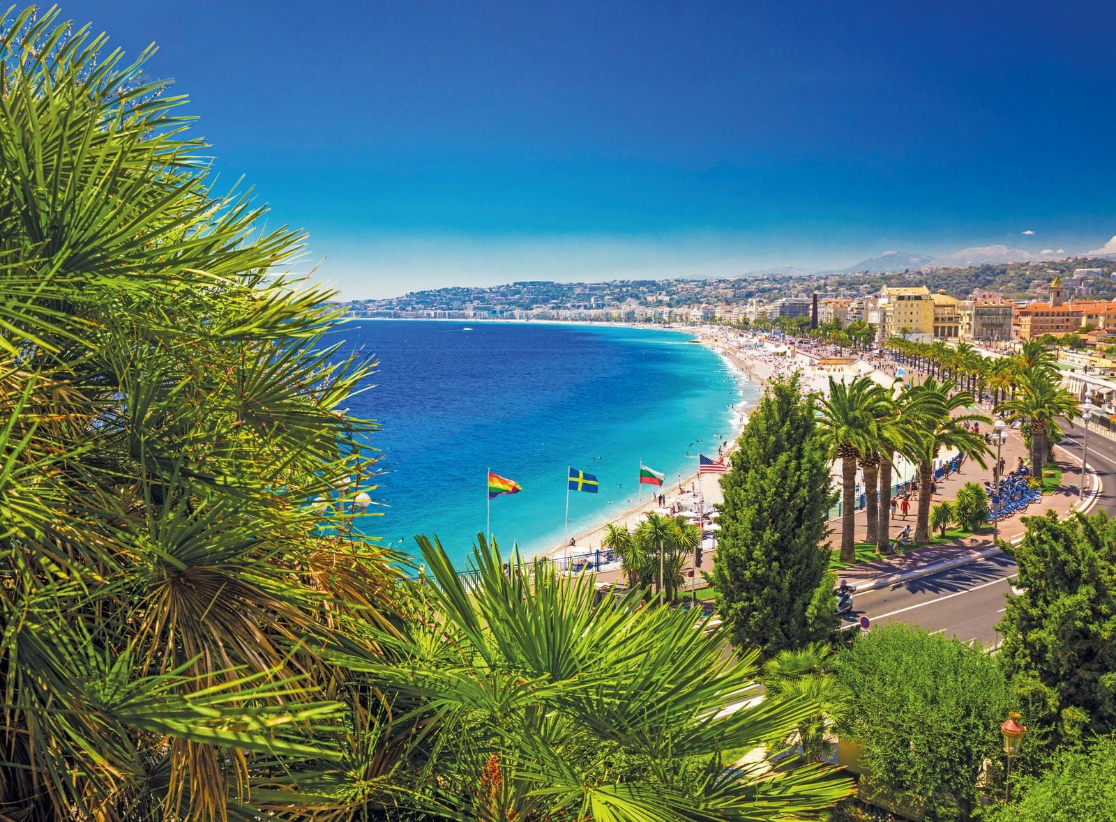 Azurblaues Wasser, Sandstrand und Palmen in Nizza, Frankreich, bei sonnigem Wetter.