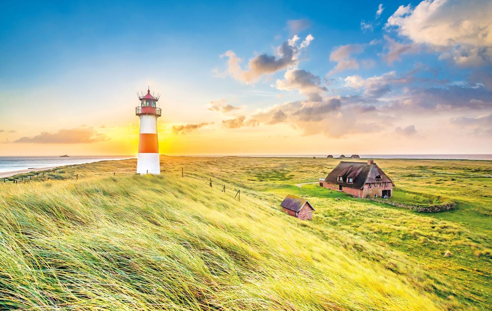 Malerischer Leuchtturm bei Sonnenuntergang auf Sylt, Deutschland, umgeben von grünen Dünen.