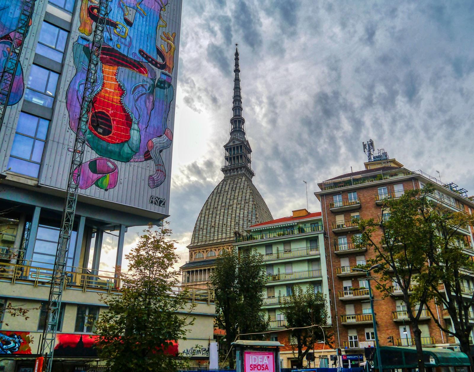 Mole Antonelliana in Turin, Italien, mit buntem Wandgemälde und bewölktem Himmel.