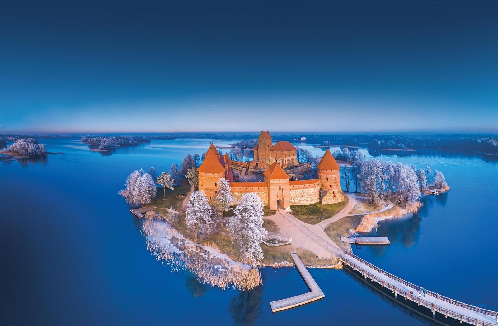 Schloss auf Insel im winterlichen See, umgeben von blauem Wasser und schneebedeckten Bäumen.
