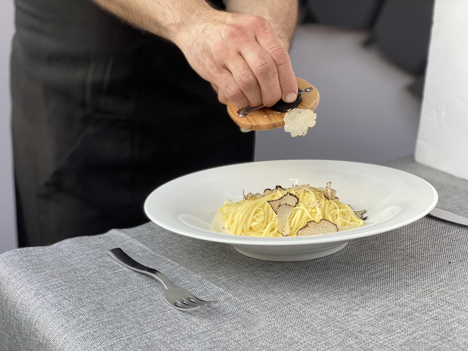 Pasta mit Trüffeln auf grauer Tischdecke, elegantes Ambiente im Restaurant.