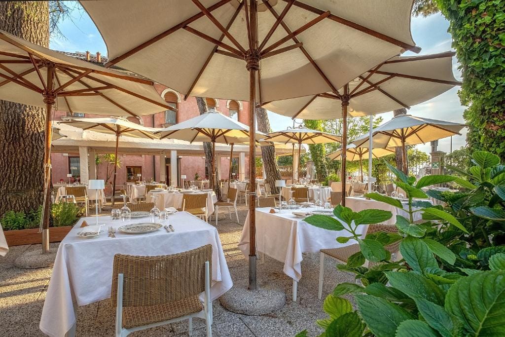 Terrasse eines Restaurants mit weißen Sonnenschirmen und gedeckten Tischen im Grünen.
