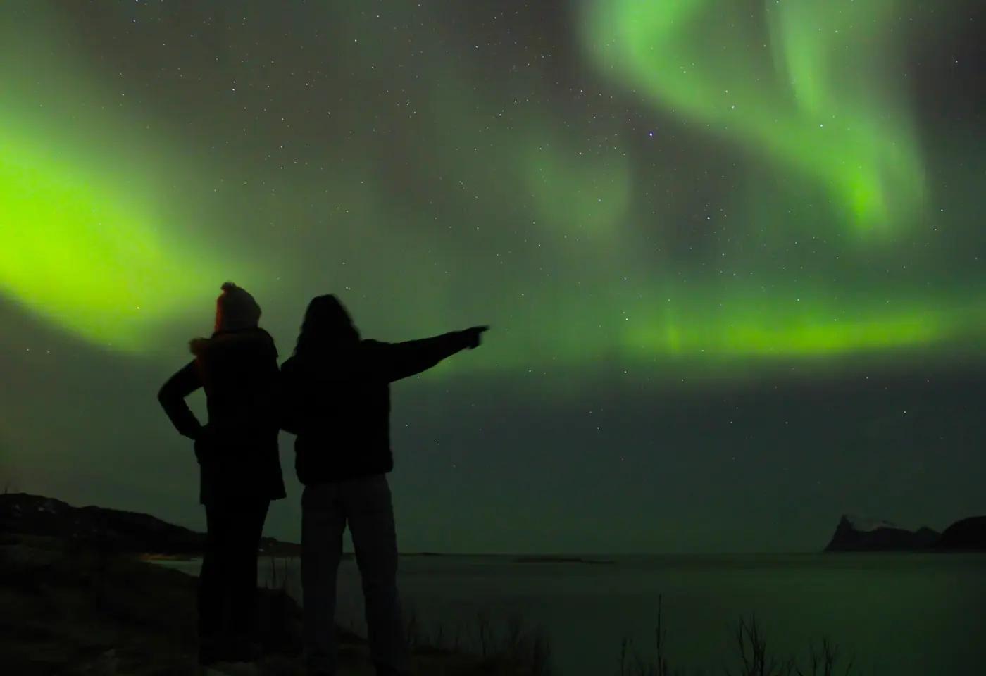 Zwei Personen beobachten das grüne Nordlicht am Nachthimmel in Norwegen.