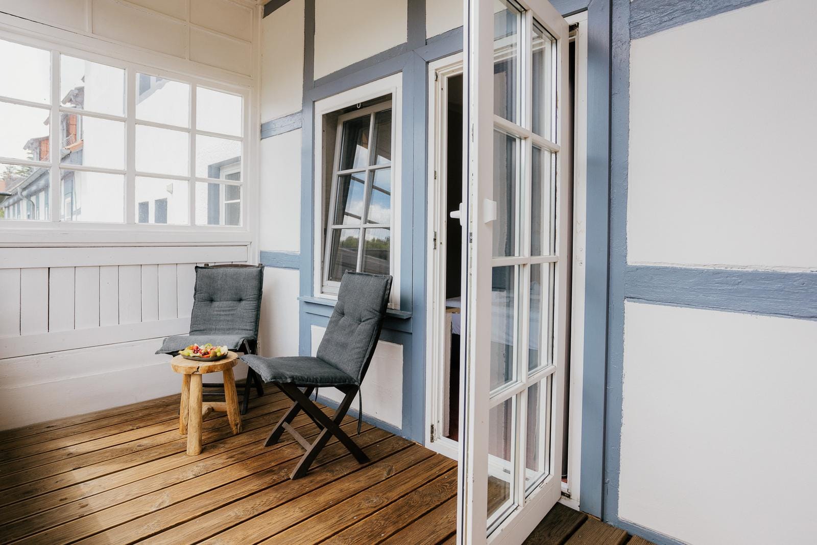 Gemütlicher Balkon mit Holzboden, zwei grauen Stühlen, Tisch mit Obst, Fachwerkstil.