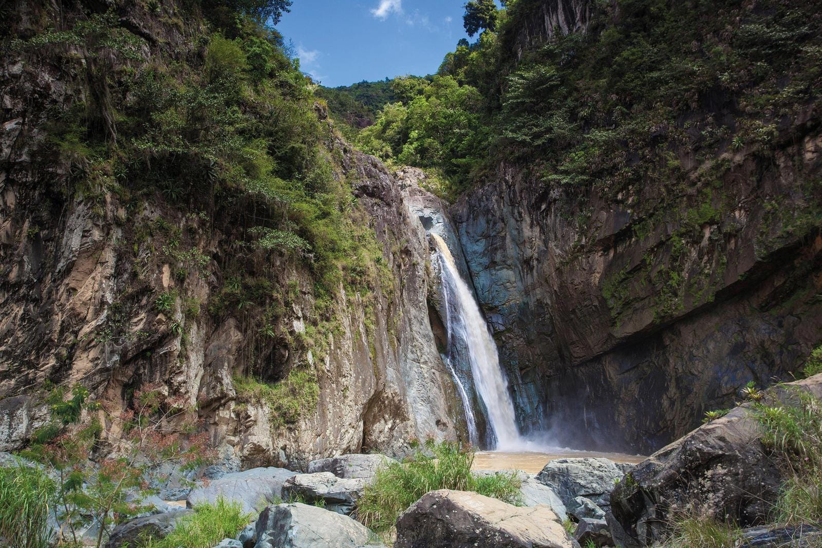 Majestätischer Wasserfall in grüner Schlucht, umgeben von Felsen und dichtem Wald.