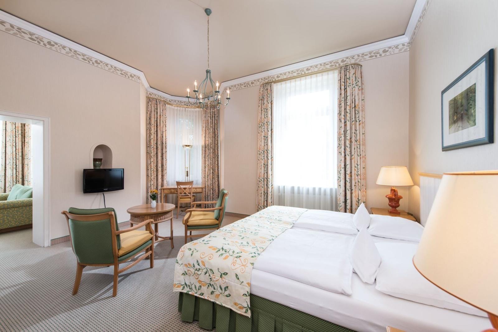 Helles Hotelzimmer im klassischen Stil mit Doppelbett, Sitzecke und dekorativen Vorhängen.