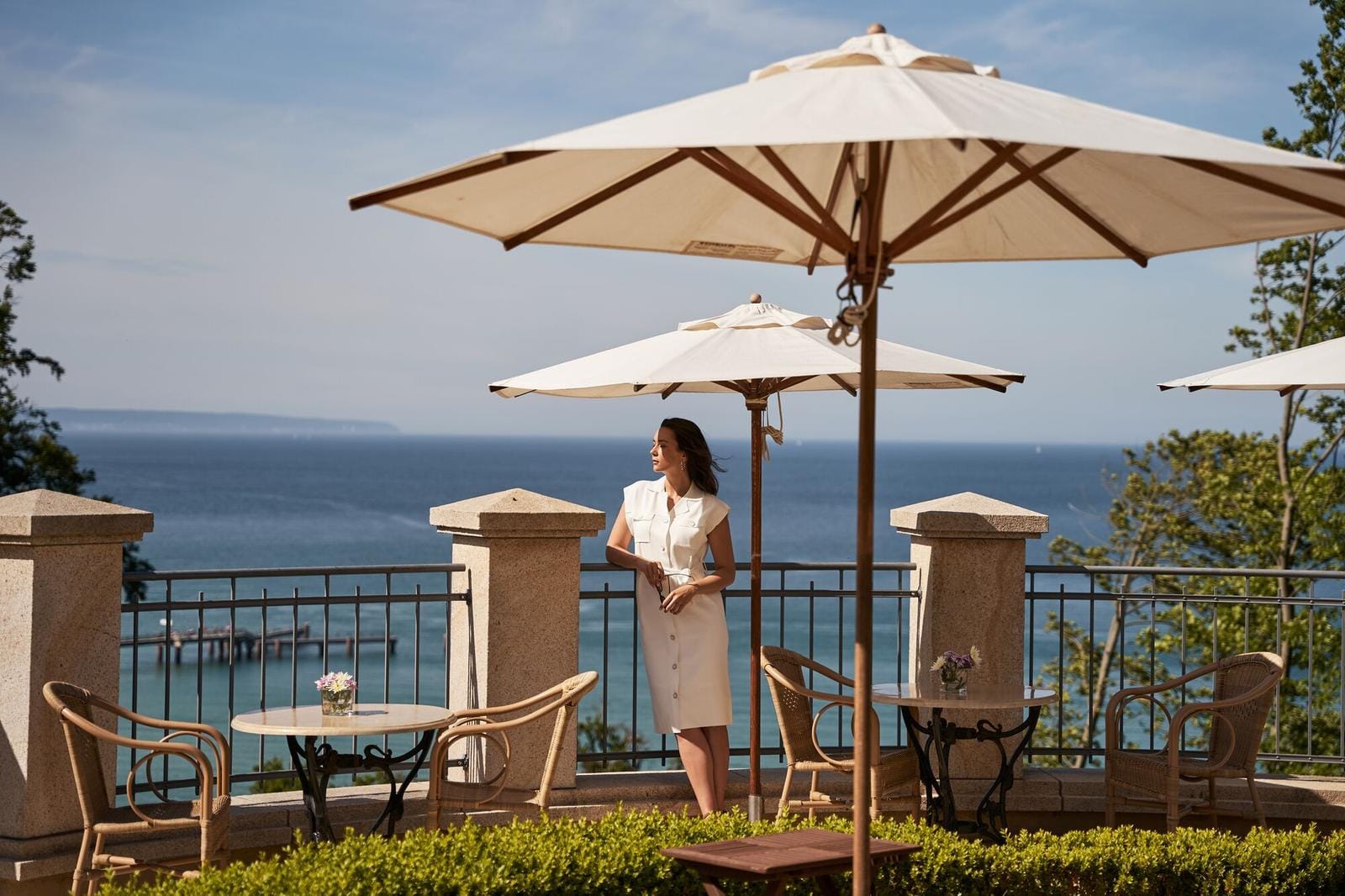 Terrasse mit Meerblick, elegante Frau, Sonnenschirme, Rattansessel, entspannte Atmosphäre.