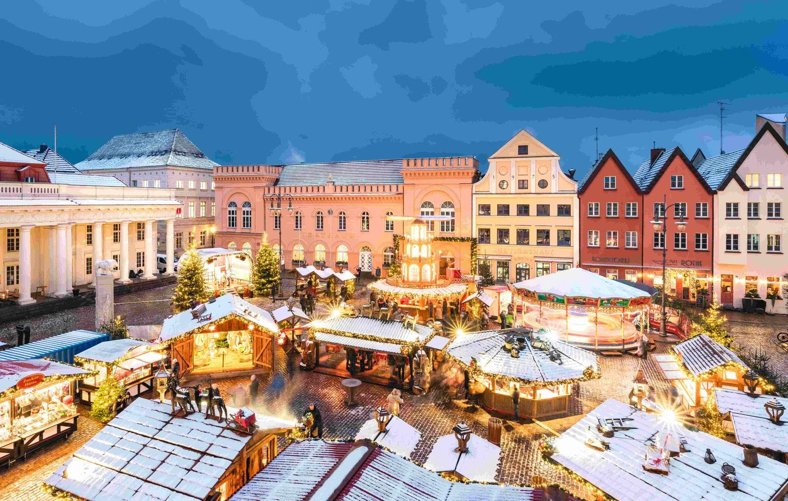 Schneebedeckter Weihnachtsmarkt in bunter Altstadt mit stimmungsvollen Lichtern.