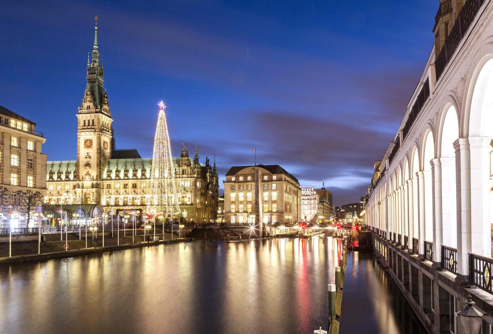 Weihnachtliches Hamburg mit beleuchtetem Rathaus und Alsterarkaden bei Nacht.