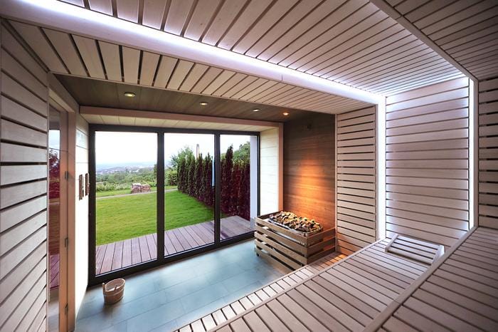 Moderne Sauna mit Holzinterieur und Panoramablick auf grünen Garten durch Glasfront.
