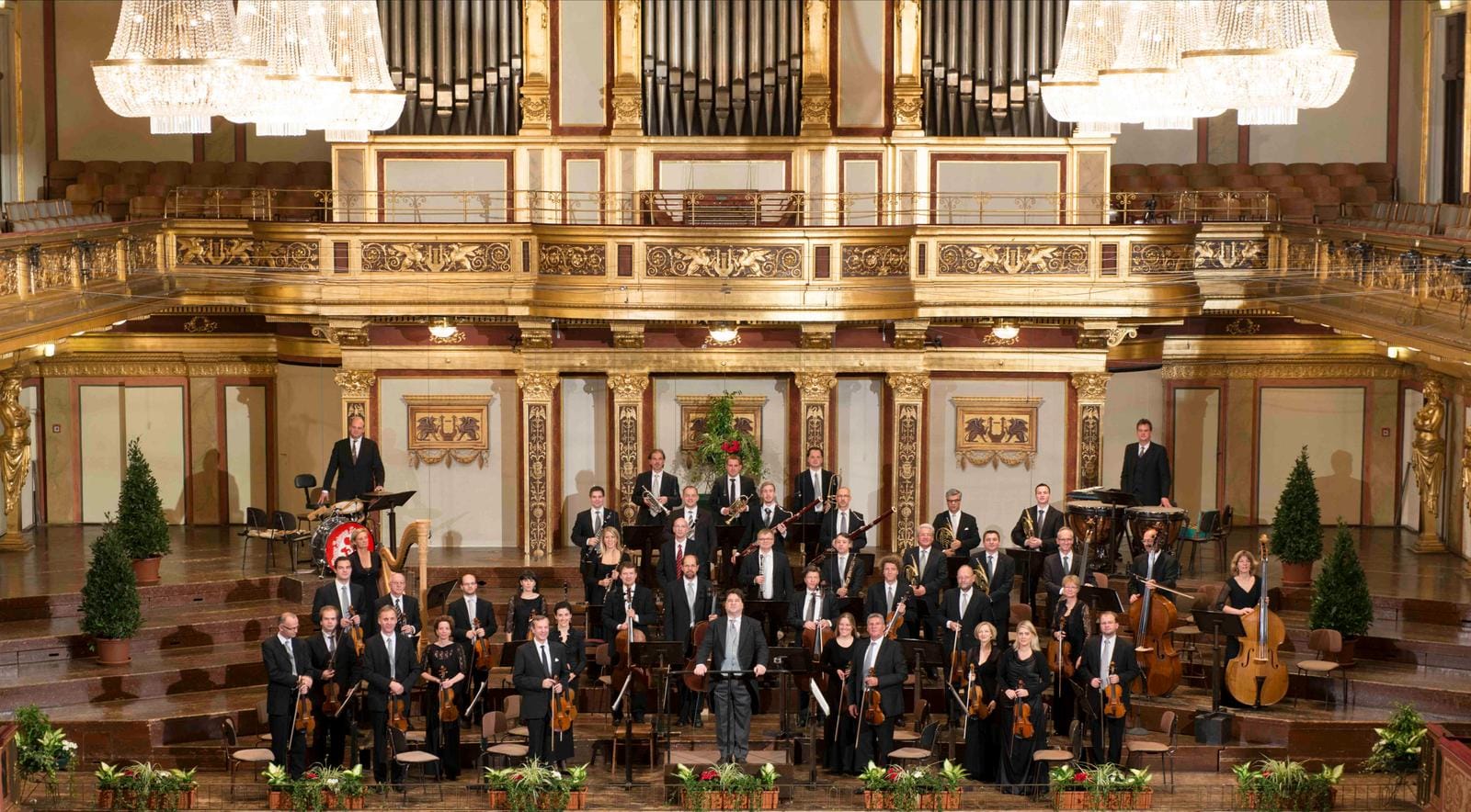 Orchester in prächtigem, goldverziertem Konzertsaal mit Kristalllüstern.