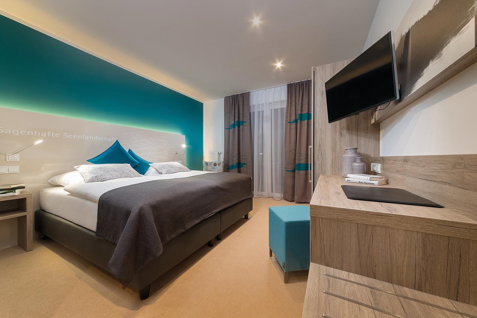 Modernes Hotelzimmer mit Doppelbett, tĂĽrkis-blauer Akzentwand und Holzdetails.