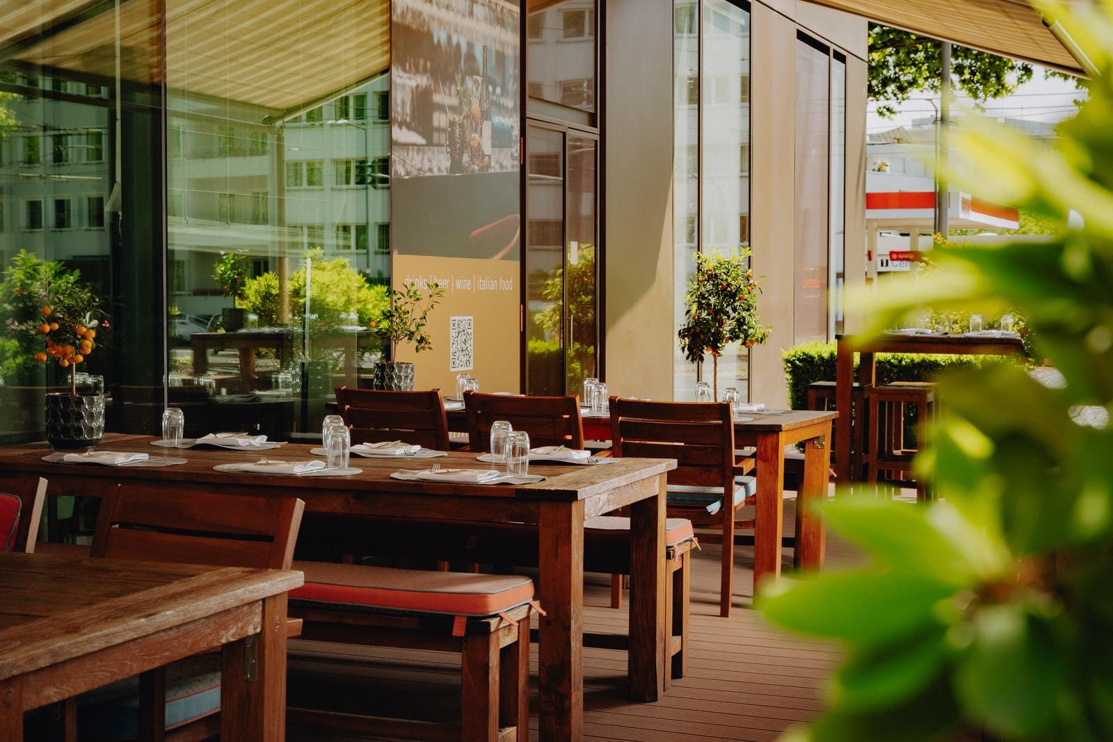 Sonnige Terrasse mit Holzmöbeln, gedeckten Tischen und Pflanzen im modernen Stil.