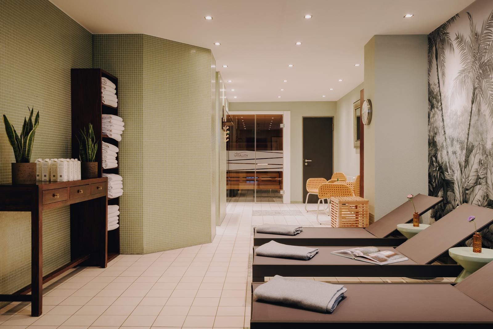 Elegantes Spa mit Liegen, grüner Wand, Sauna, Pflanzen und gemütlichem Ambiente.