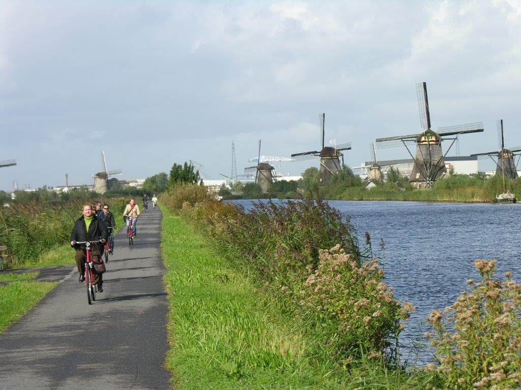 Radfahrer in den Niederlanden vor malerischen Windmühlen entlang eines Kanals.