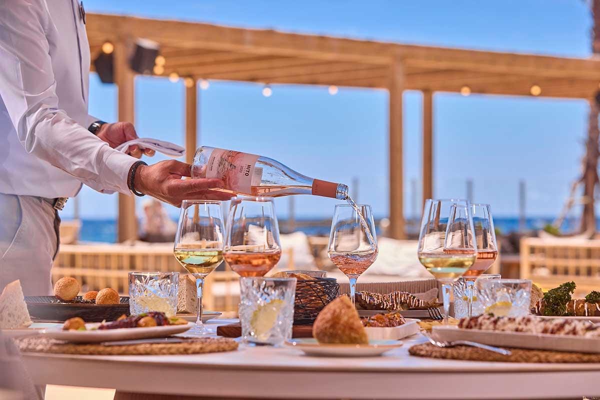 Ein Kellner serviert Wein im Strandrestaurant mit elegant gedecktem Tisch.