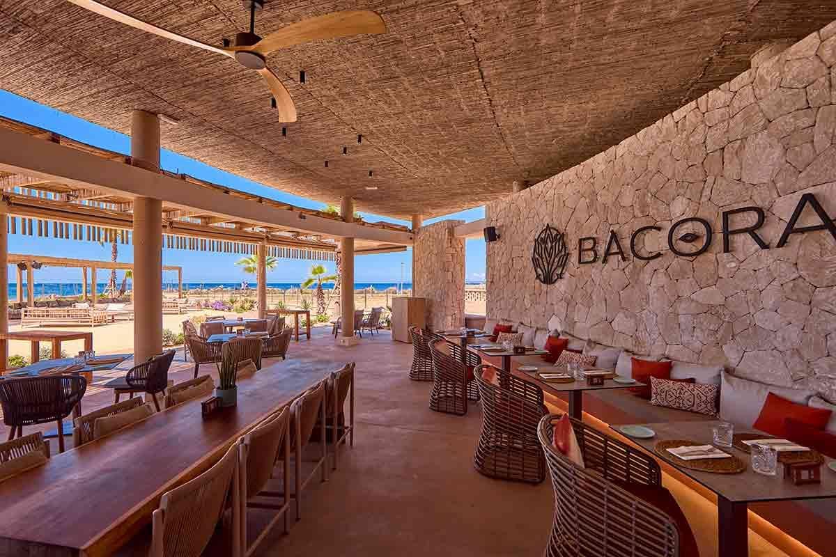 Offenes Restaurant am Meer, Holzdecken, Steinwände, moderne Rattanmöbel, entspannte Atmosphäre.