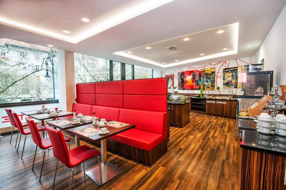 Modernes Hotelrestaurant mit roten SitzbĂ€nken, Holzboden und groĂen Fenstern.