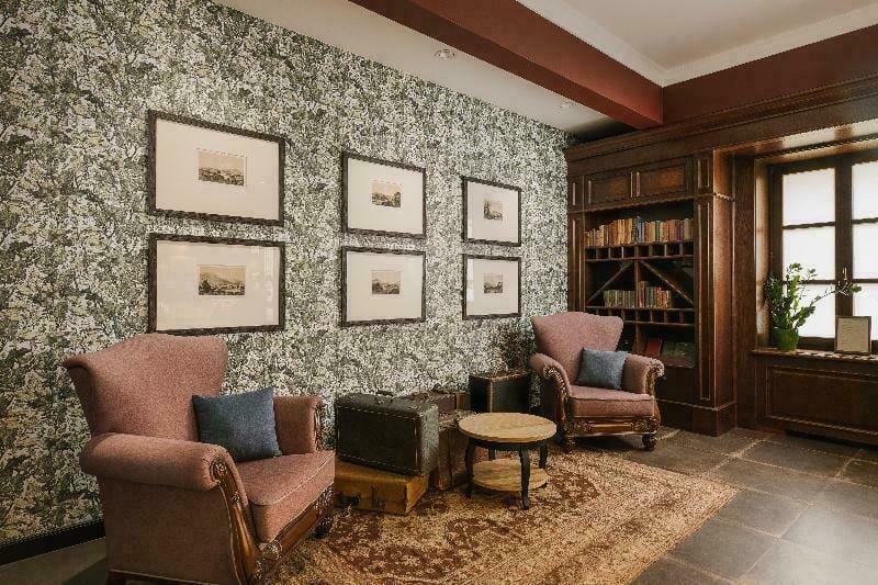 Gemütliche Hotel-Lounge mit vintage Sesseln, Bücherregal und gemusterten Wänden.