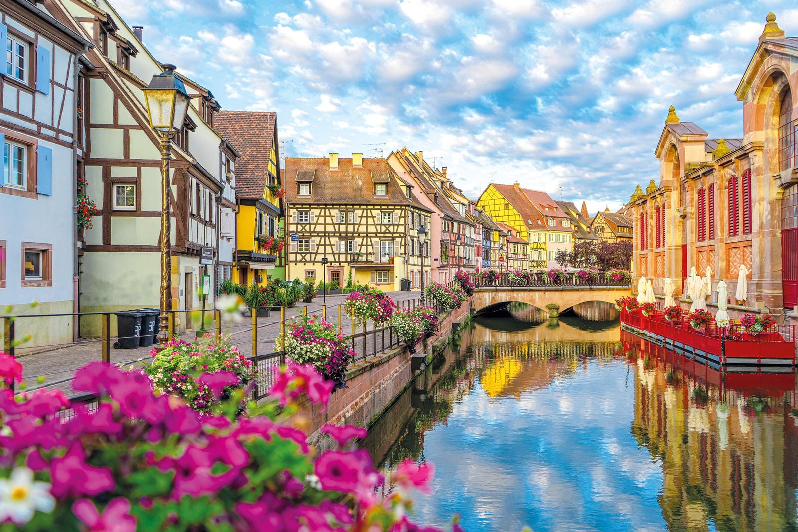 Malerischer Kanal in Colmar, Frankreich, mit Fachwerkhäusern und blühenden Blumen.
