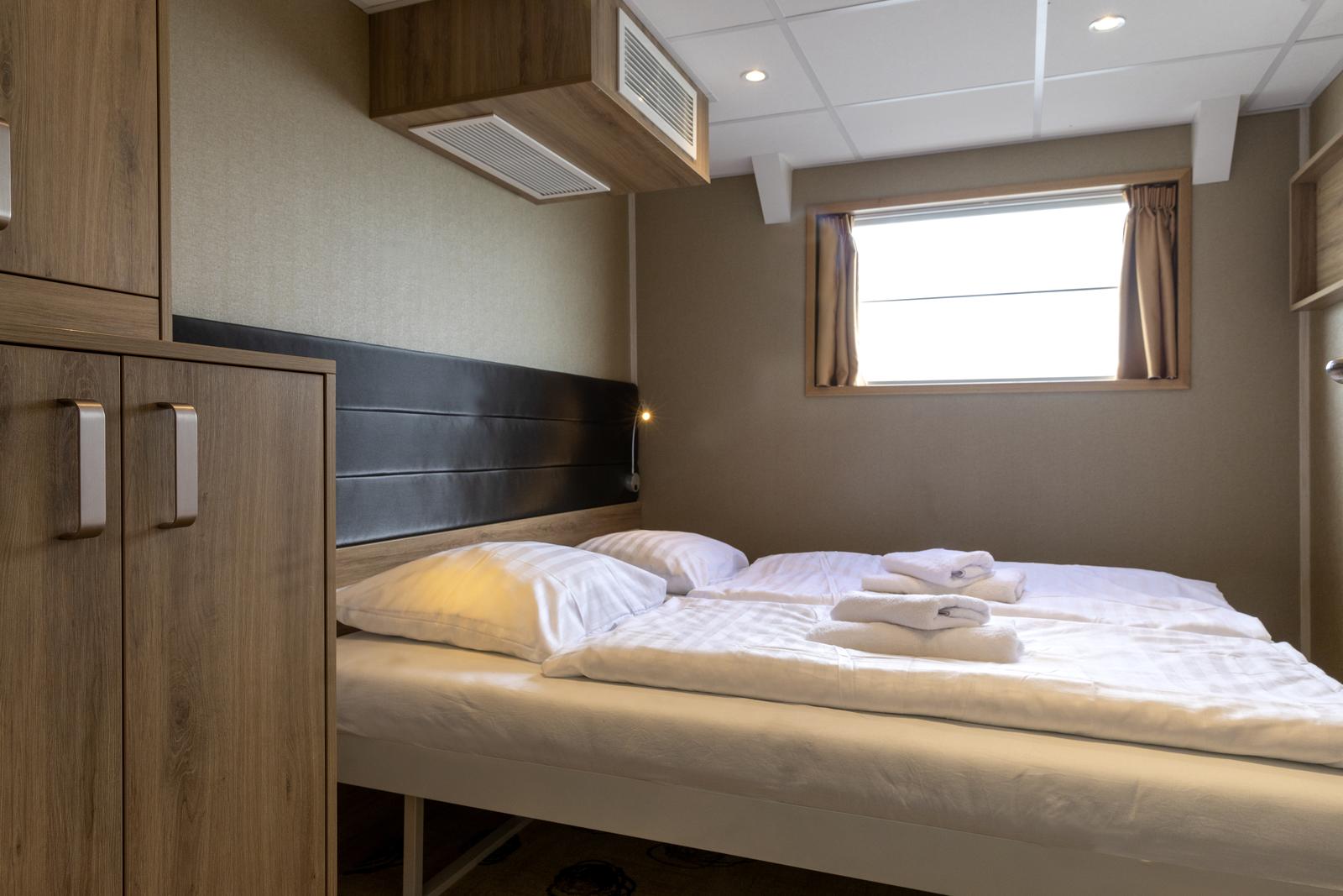 Komfortables Doppelzimmer mit Holzmöbeln, weißem Bettzeug und kleinem Fenster.