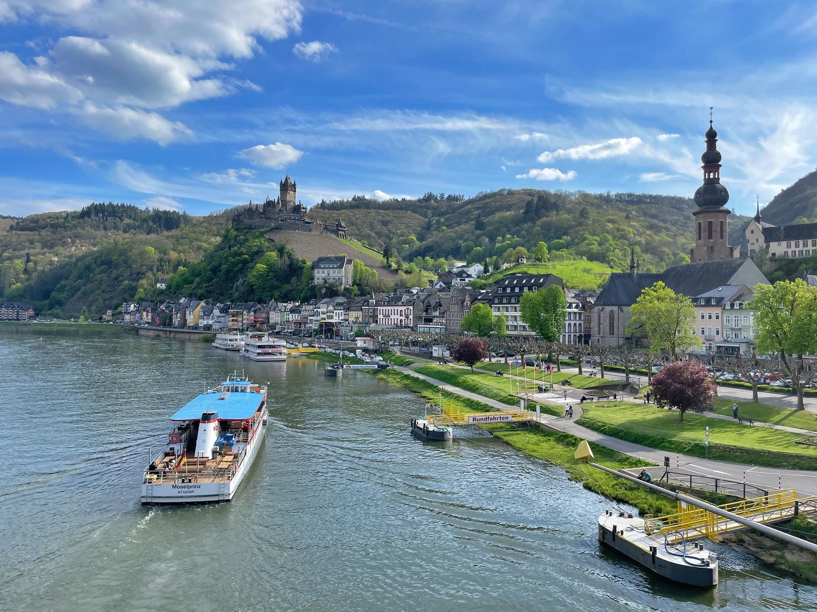 Blick auf Cochem an der Mosel mit Reichsburg und Kirche, Schiff auf dem Fluss, sonniger Tag.