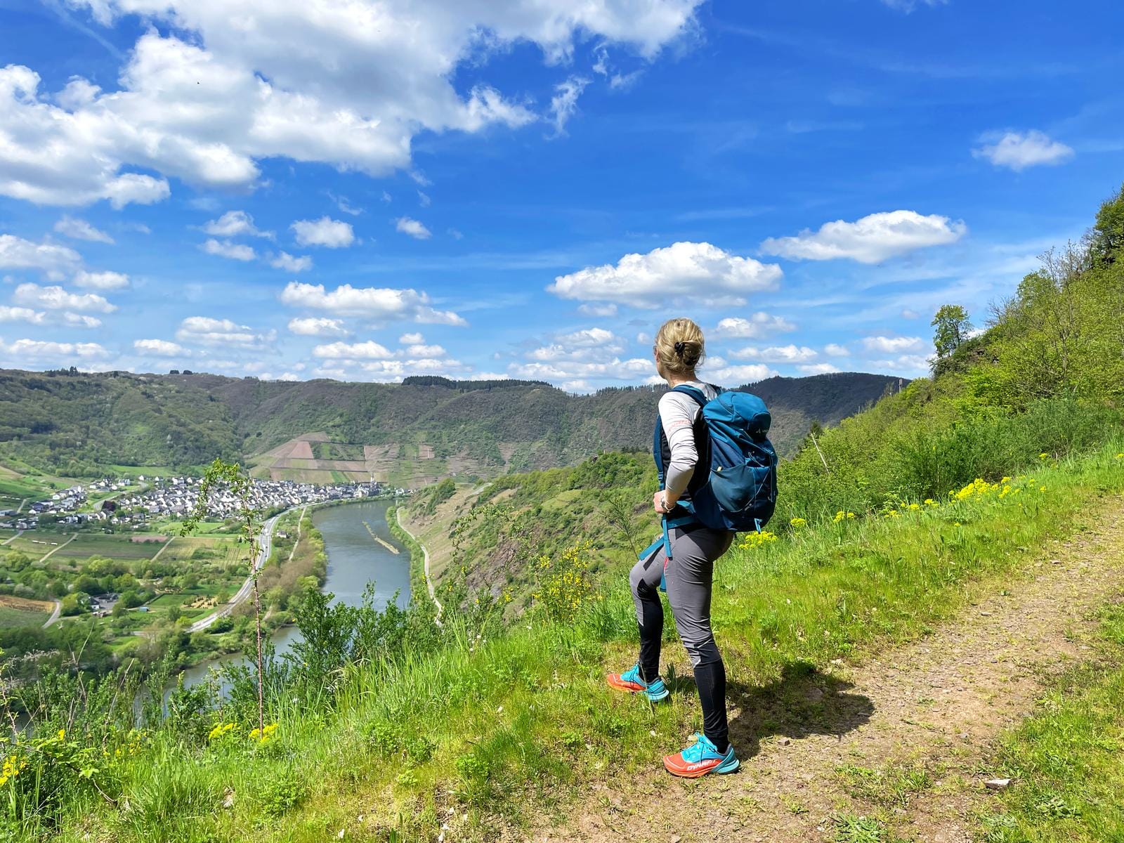 Wanderin blickt auf grünes Moseltal bei klarem Himmel und bunter Stadt.