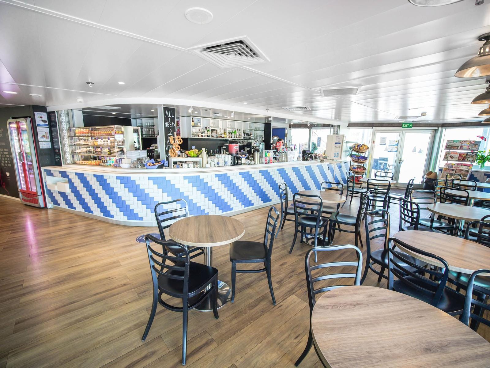 Helle Hotelbar mit blau-weißer Theke, Holzboden und schwarzen Stühlen.