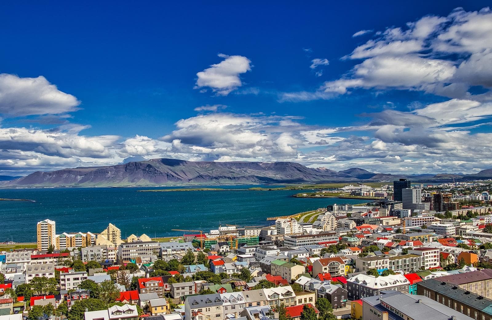 Panorama von ReykjavĂk, Island mit bunten Häusern vor Bergen und blauem Himmel.