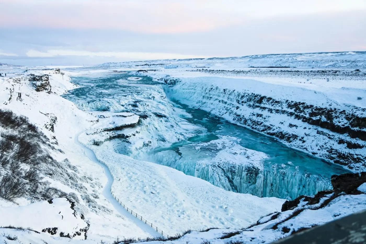 Verschneiter Gullfoss-Wasserfall in Islands Winterlandschaft, mit gefrorenem Fluss.