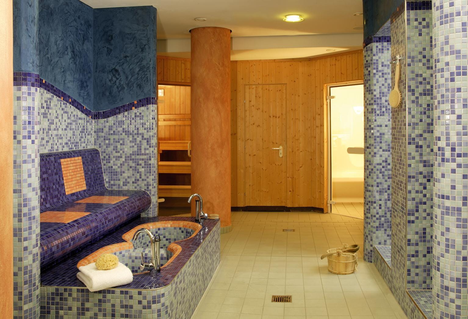 Wellnessbereich mit blauen Mosaikfliesen, Holzsauna und entspannendem Ambiente.