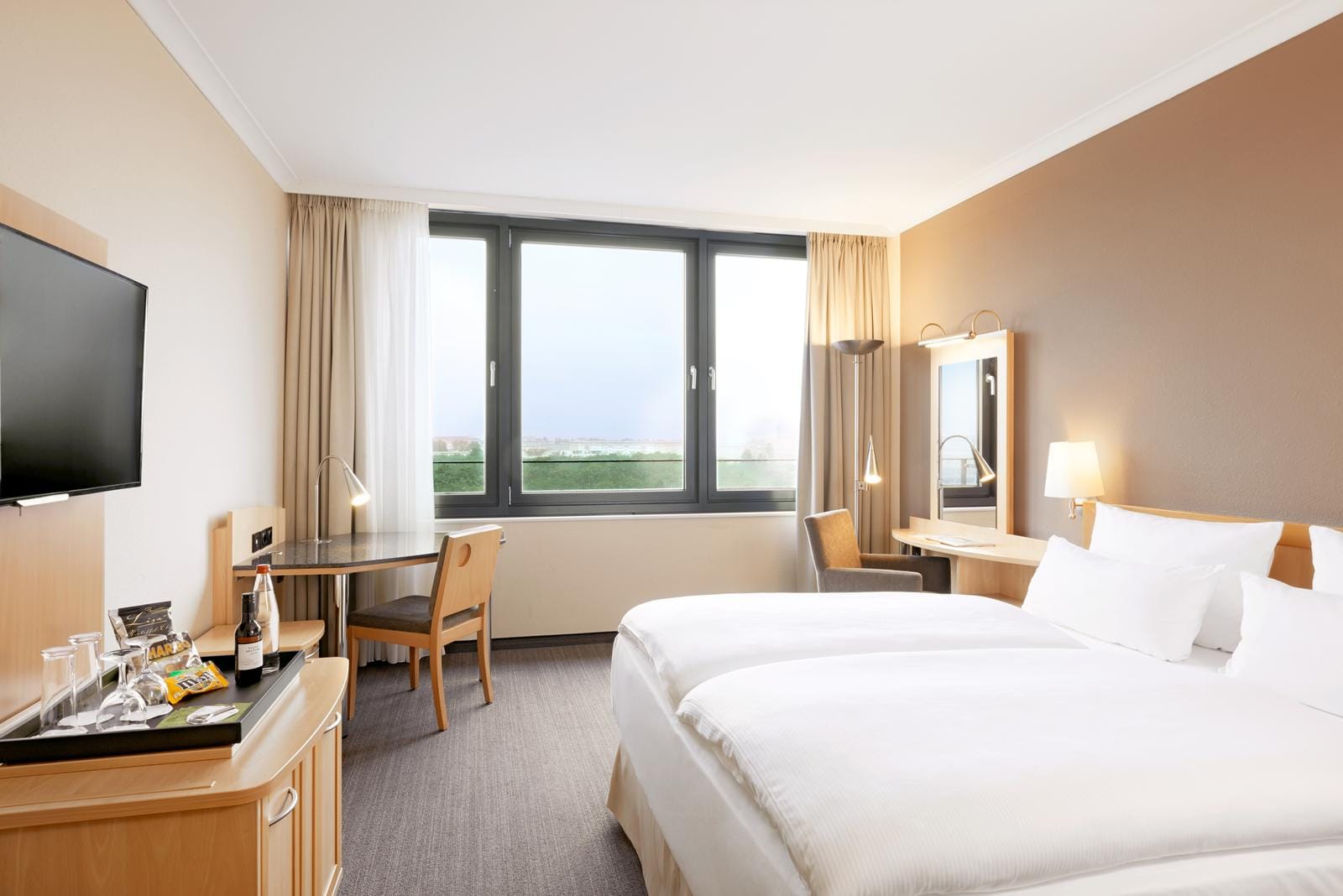 Modernes Hotelzimmer mit zwei weißen Betten, Schreibtisch und großem Fenster.