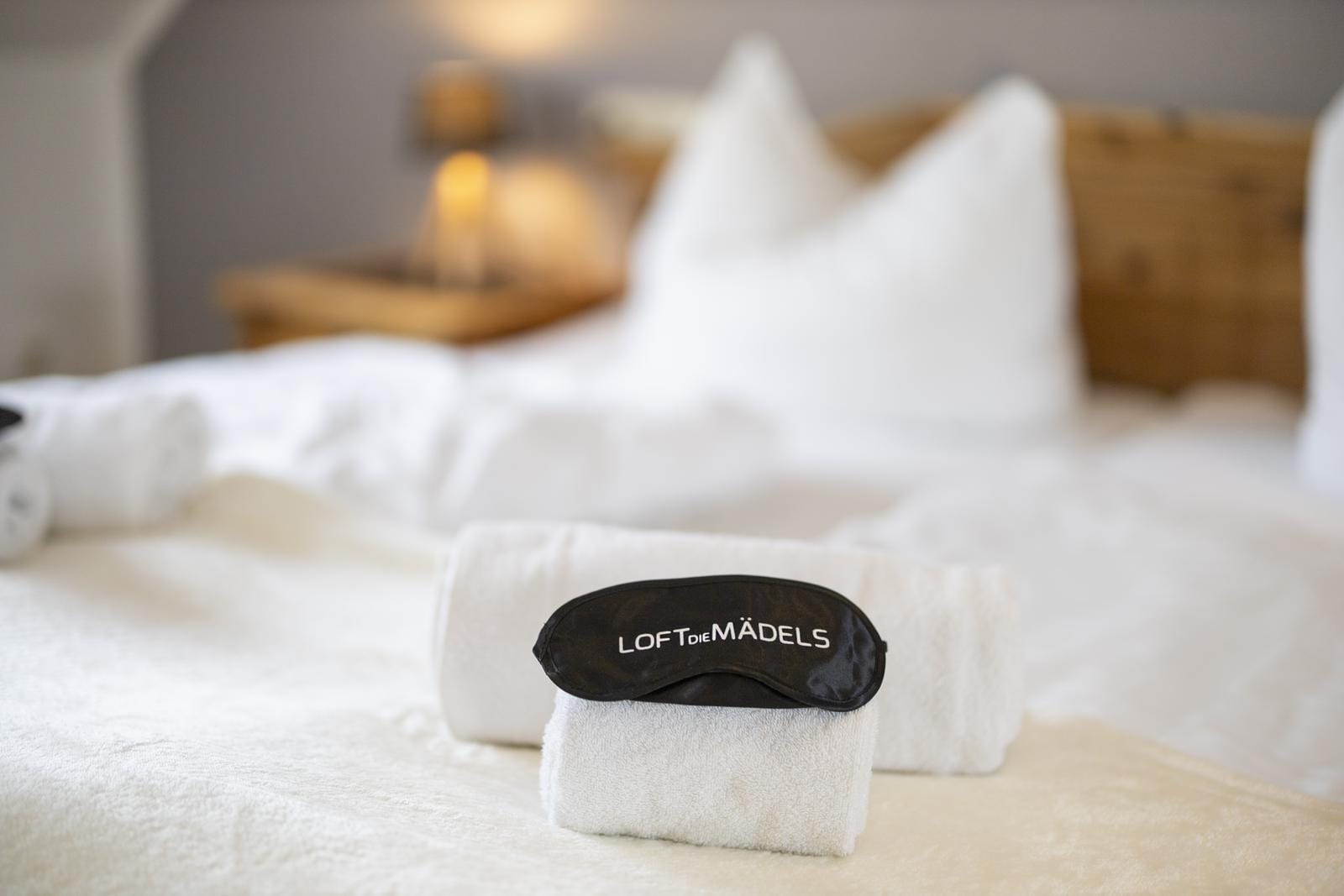 Gemütliches Hotelzimmer mit weißen Handtüchern, Schlafmaske und warmer Beleuchtung.